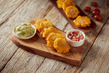 Patacones or tostones, typical Ecuadorian appetizer that consists on fried green plantain slices. It’s accompanied with guacamole and served on a traditional plate with a wooden and rustic background. - obrazy, fototapety, plakaty