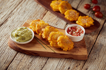 Patacones or tostones, typical Ecuadorian appetizer that consists on fried green plantain slices. It’s accompanied with guacamole and served on a traditional plate with a wooden and rustic background. - obrazy, fototapety, plakaty