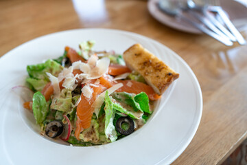 fresh Salmon salad with fresh green leaves and black olive on white plate.