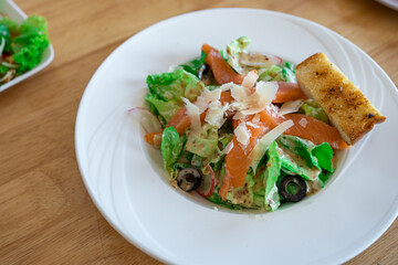 fresh Salmon salad with fresh green leaves and black olive on white plate.