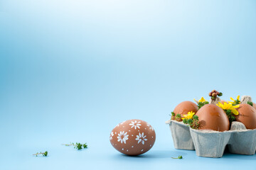 chicken eggs in a tray on a blue background with flowers, holiday concept, space for text