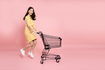 Full length portrait of young Asian woman jumping and pushing an empty shopping cart or shopping...