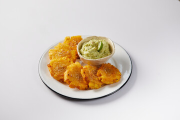 Patacones or tostones, typical Ecuadorian appetizer that consists on fried green plantain slices. It’s accompanied with guacamole and served on a traditional plate with a white background. 