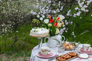 Tea time with cake and cookies in the spring garden outdoors. The table is covered with a floral tablecloth. In english style