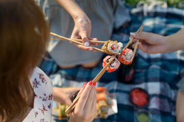 Three hands with chopsticks and sushi. Top view - obrazy, fototapety, plakaty