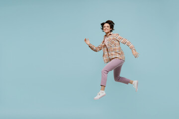 Fototapeta na wymiar Full body side profile view young smiling happy woman 20s wearing casual brown shirt run fast jump high isolated on pastel plain light blue color background studio portrait. People lifestyle concept.