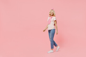 Full body smiling cheerful fun cool elderly happy woman 50s wear t-shirt birthday hat look camera walking going strolling isolated on plain pastel pink background. Celebrating party holiday concept
