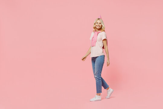 Full body smiling cheerful fun cool elderly happy woman 50s wear t-shirt birthday hat look camera walking going strolling isolated on plain pastel pink background. Celebrating party holiday concept