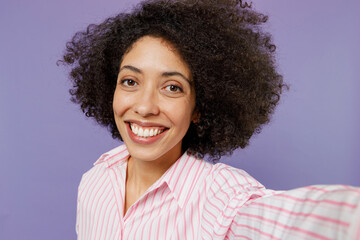 Close up young smiling happy fun woman of African American ethnicity 20s wear pink striped shirt doing selfie shot pov on mobile phone isolated on plain pastel light purple background studio portrait.