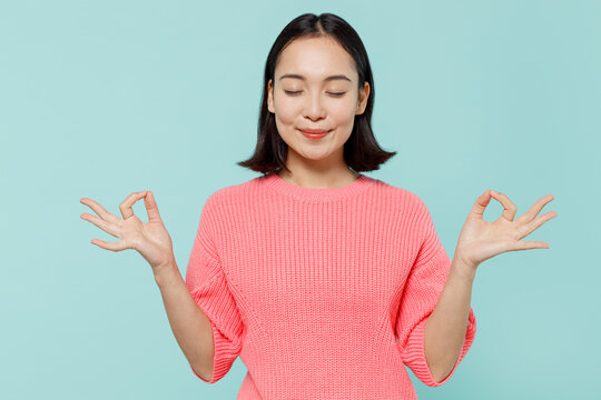 Young Spiritual Happy Woman Of Asian Ethnicity 20s Wear Pink Sweater Hold Spreading Hands In Yoga Om Aum Gesture Relax Meditate Try To Calm Down Isolated On Pastel Plain Light Blue Color Background