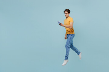 Full body side view caucasian smiling young man 20s wear yellow t-shirt jump high use hold mobile...