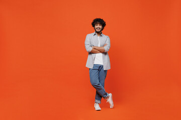 Full size body length confident happy young bearded Indian man 20s years old wears blue shirt hold hands crossed isolated on plain orange background studio portrait. People emotions lifestyle concept. - obrazy, fototapety, plakaty