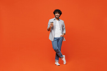 Full size body length fascinating young bearded Indian man 20s years old wears blue shirt hold takeaway delivery craft paper brown cup coffee to go isolated on plain orange background studio portrait. - obrazy, fototapety, plakaty