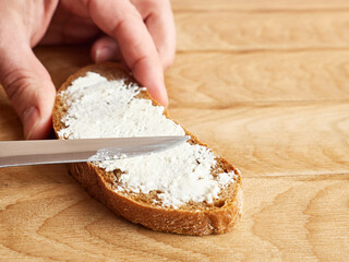 Spread sour milk cheese on a slice of bread with a knife.
