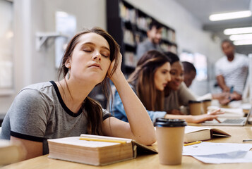 Im just closing my eyes for a bit. Shot of a young woman looking tired while studying in a college library in the library.