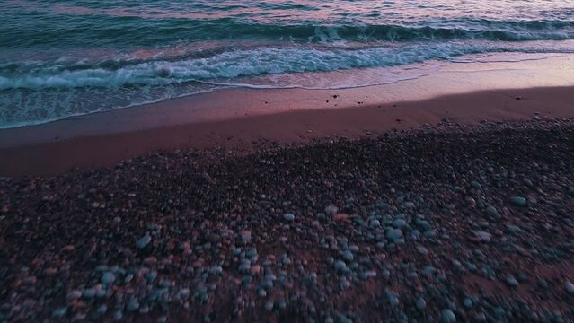 Entrando al mar desde la playa con piedras con olas y espuma y un plano del atardecer con las nubes en el cielo
