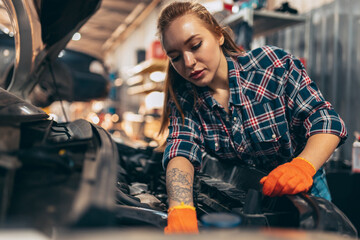 Female auto mechanic. beautiful young red-headed girl in working process at auto service station, indoors. Gender equality. Work, occupation, fashion, job