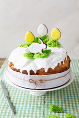 Easter cake with raisins decorated with white icing and gingerbread in the shape of Easter eggs and a rabbit on green grass on a green checkered tablecloth. Vertical orientation.
