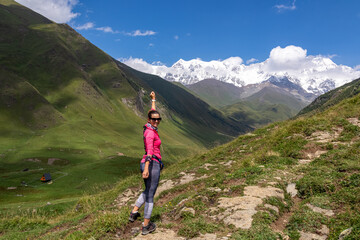 Fototapeta na wymiar A female backpacker on a hiking trail to Chubedishi viewpoint. There is an amazing view on the Shkhara Glacier,near the village Ushguli the Greater Caucasus Mountain Range in Georgia, Svaneti Region