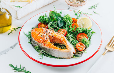 Grilled Salmon steak and fresh vegetable salad with a lemon over white marble background. Healty food concept