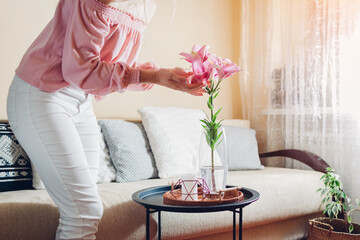 Woman enjoying lily flowers in vase at home. Young housewife admires bouquet of fresh blooms....