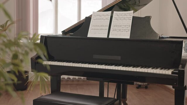 Slowmo of black grand piano and two sheets of paper with notes on it standing in class of music school