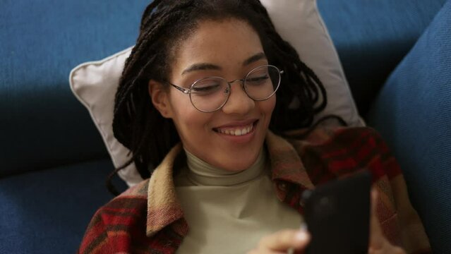 Happy african american teen relaxing on sofa at home with smartphone