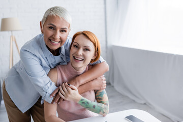 excited and happy lesbian couple looking at camera at home