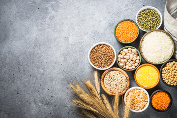 Gluten free cereals. Different bowls with rice, buckwheat, corn, lentils, soy beans and quinoa at stone table. Top view with copy space.