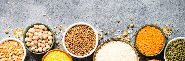 Gluten free cereals. Different bowls with rice, buckwheat, corn, lentils, soy beans and quinoa at stone table. Long banner format.