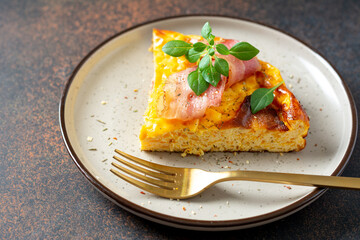 A piece of frittata with pumpkin, bacon and ricotta in a ceramic plate on a dark culinary background. Traditional Italian delicious homemade egg dish on the kitchen table