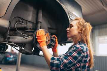 Car reapir. Young red-headed girl, auto mechanic working at auto service station using different...