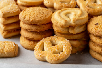 Fototapeta na wymiar Sugar pretzel against of stacked shortbread cookies on a white baking parchment. Assorted crispy butter biscuits close-up. Tasty baked pastry. Breakfast, snack and sweet food concepts.