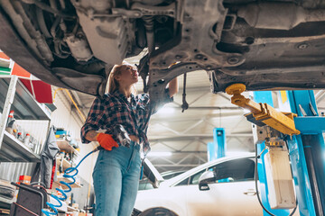 Destroying gender stereotypes. Young woman auto mechanic working at auto service station using...