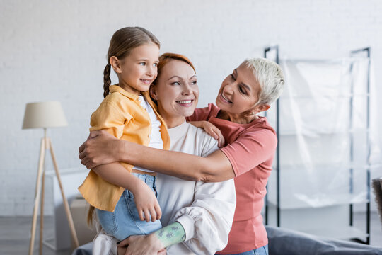 cheerful lesbian woman embracing girlfriend with adopted daughter in new home - Powered by Adobe