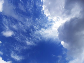 Obraz premium Lush clouds overhead in the sky block the sunlight. Through the layers of clouds, a blue sky peeks through. Horizontal photo.