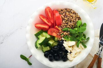 Healthy vegetable lunch from the Buddha bowl with with tomato, cucumber, mozzarella cheese, quinoa, olives and microgreens. Vegan salad buddha bowl. Healthy and balanced food concept.