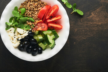 Vegetarian Vegan salad bowl or buddha bowl with tomato, cucumber, mozzarella cheese, quinoa, olives and microgreens. Healthy and balanced food concept on old wooden dark background Top view copy space