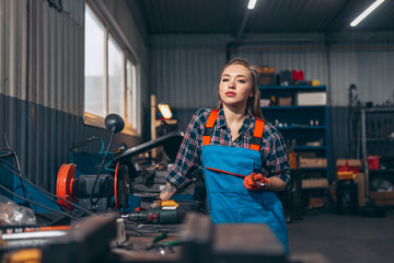 Portrait of young confident girl wearing working clothes standing at auto service station, indoors. Gender equality. Emotions, work, occupation, fashion, job and hobby