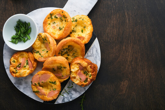 Delicious egg muffins with green onions, bacon, cheese and tomatoes on wooden board on old wooden rustic background. Healthy high protein and low carb breakfast. Homemade food.