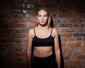 Young beautiful woman dressed in sportswear posing against a red brick wall.