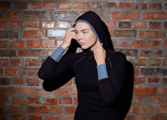 Fototapeta na wymiar Young fit pretty woman dressed in sport clothes poses against brick wall.