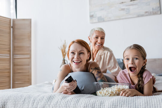 Excited kid watching movie near popcorn and mothers on bed