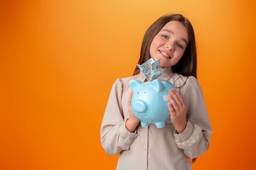 Teen girl with piggy bank on orange color background.