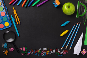 Black chalkboard school background with school supplies and stationery items, empty copy space for text