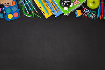 Black chalkboard school background with school supplies and stationery items, empty copy space for...