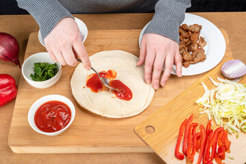 Woman smears pita with ketchup with a spoon.