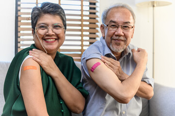 Healthy Asian senior couple showing bandage plaster on arm after received covid vaccination for prevent covid-19 infection. Coronavirus pandemic protection health care senior lifestyle concept.