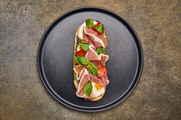 Flat lay bruschetta with mozzarella, Parma ham and pesto on black plate on textured background