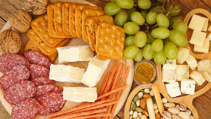 Different tasty appetizers on wooden background, top view. Snacks for wine. Cheese and meat plate. Sausages, cheese, nuts, grapes, crackers